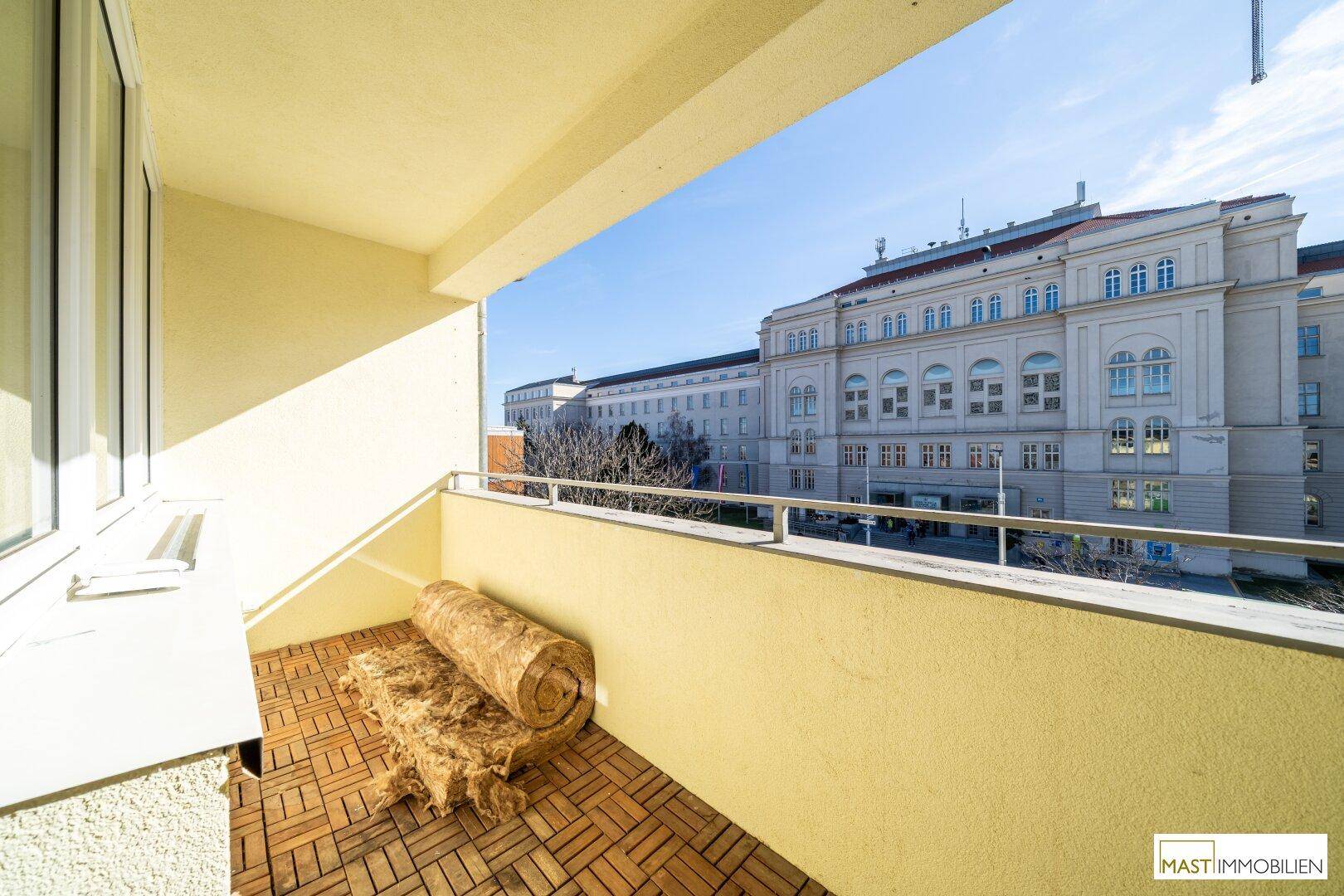 Geräumiger Balkon mit Holzboden und freiem Blick auf die umliegende Stadtarchitektur.