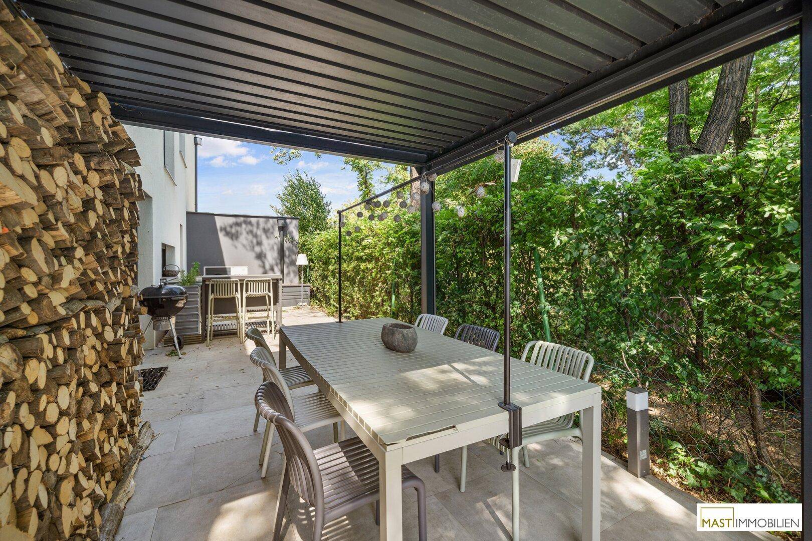 Überdachte Terrasse mit großem Esstisch, Grillbereich und Holzstapel.