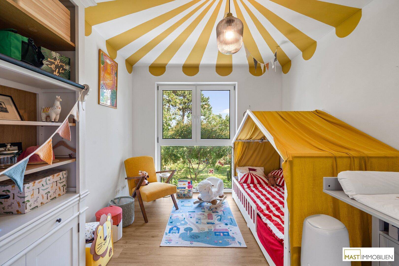 Farbenfrohes Kinderzimmer mit Zirkuszelt-Bett, Spielbereich und Blick ins Grüne.