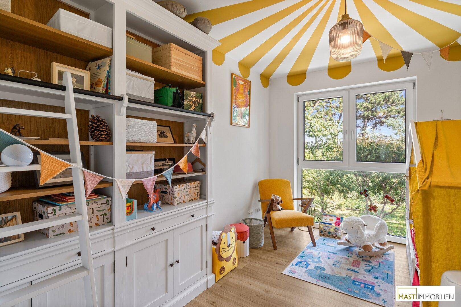 Helles Kinderzimmer mit Spielzeug, Bücherregal und Blick in den Garten.
