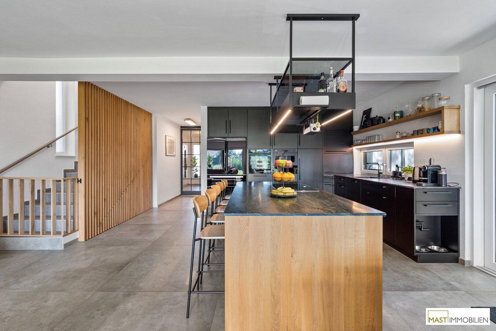 Offene Küche mit Kochinsel und Holzlamellenwand, die den Treppenbereich elegant abtrennt.