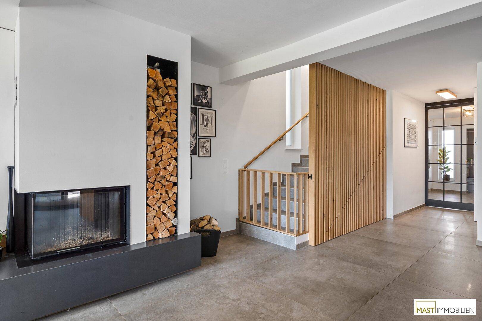 Eingangsbereich mit modernem Kamin, integriertem Holzregal und eleganter Holzlamellenwand neben der Treppe.