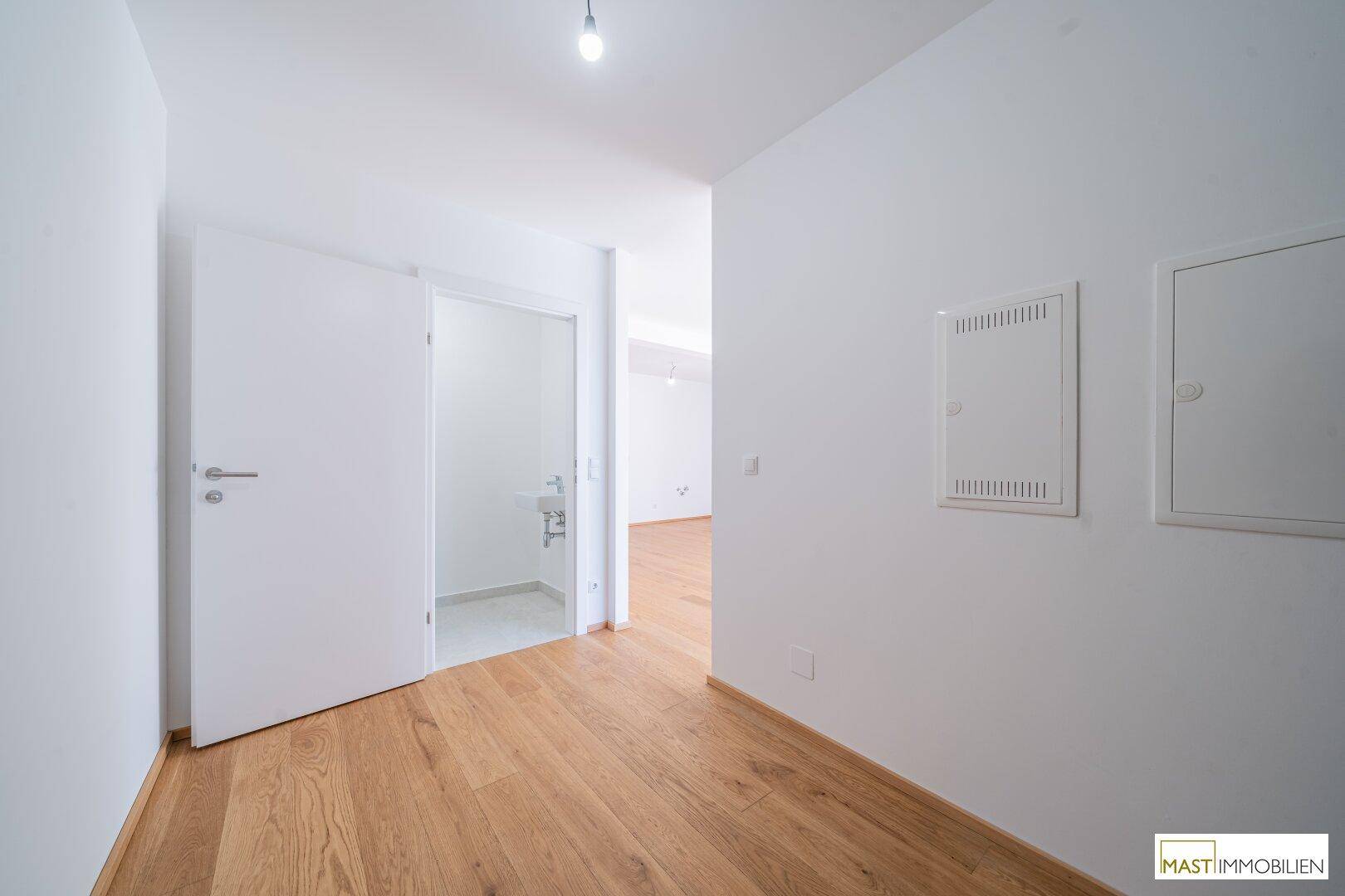 Heller Flur mit Holzparkettboden und Zugang zu einem Gäste-WC.