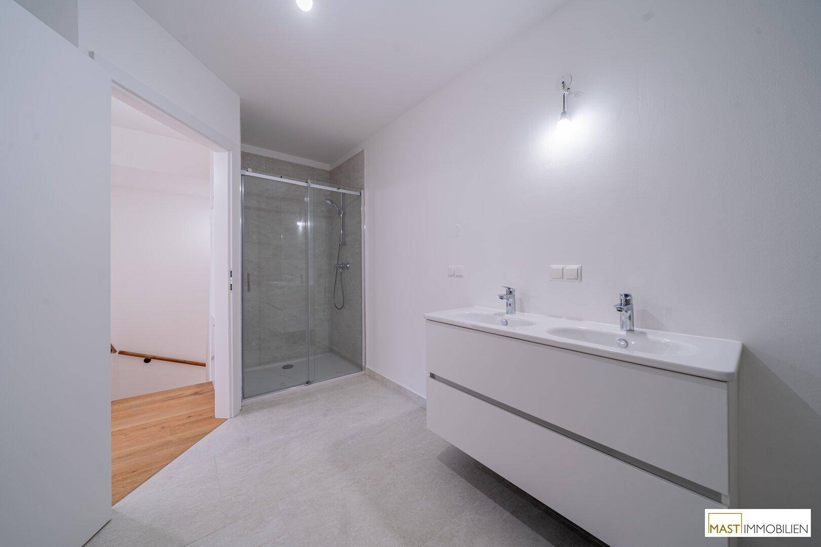 Modernes Badezimmer mit Doppelwaschbecken, großer Duschkabine und hellen Fliesen.