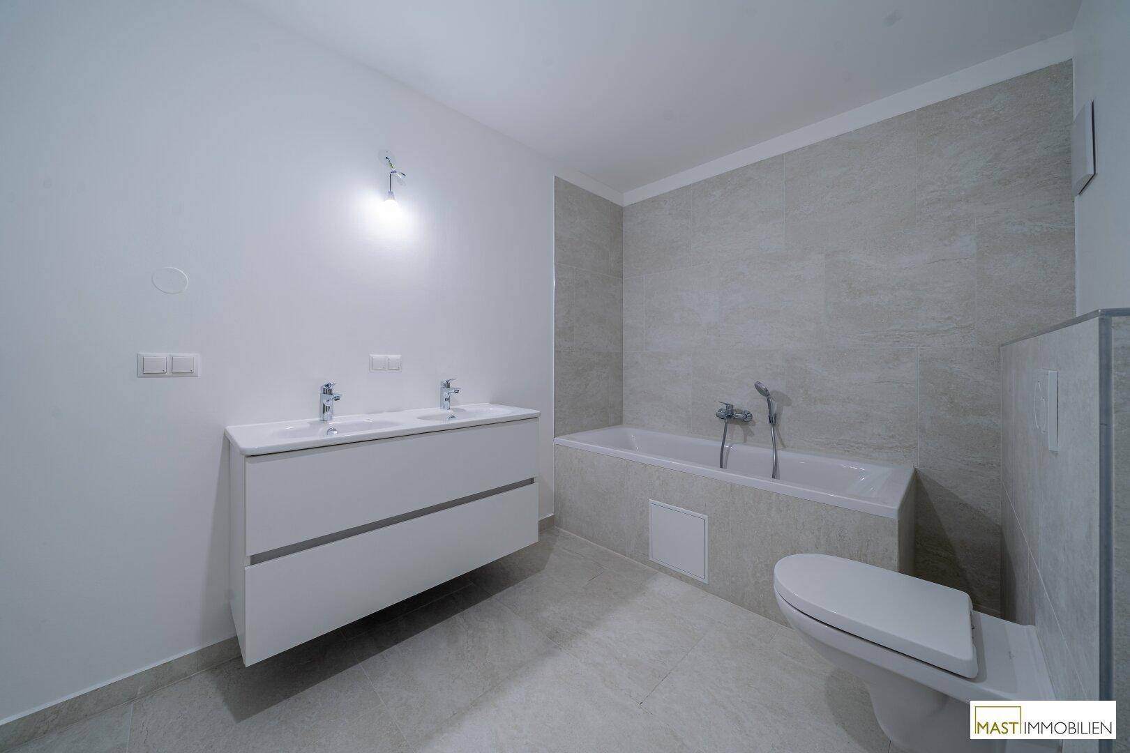 Geräumiges Badezimmer mit Doppelwaschbecken, Badewanne und wandmontierter Toilette.