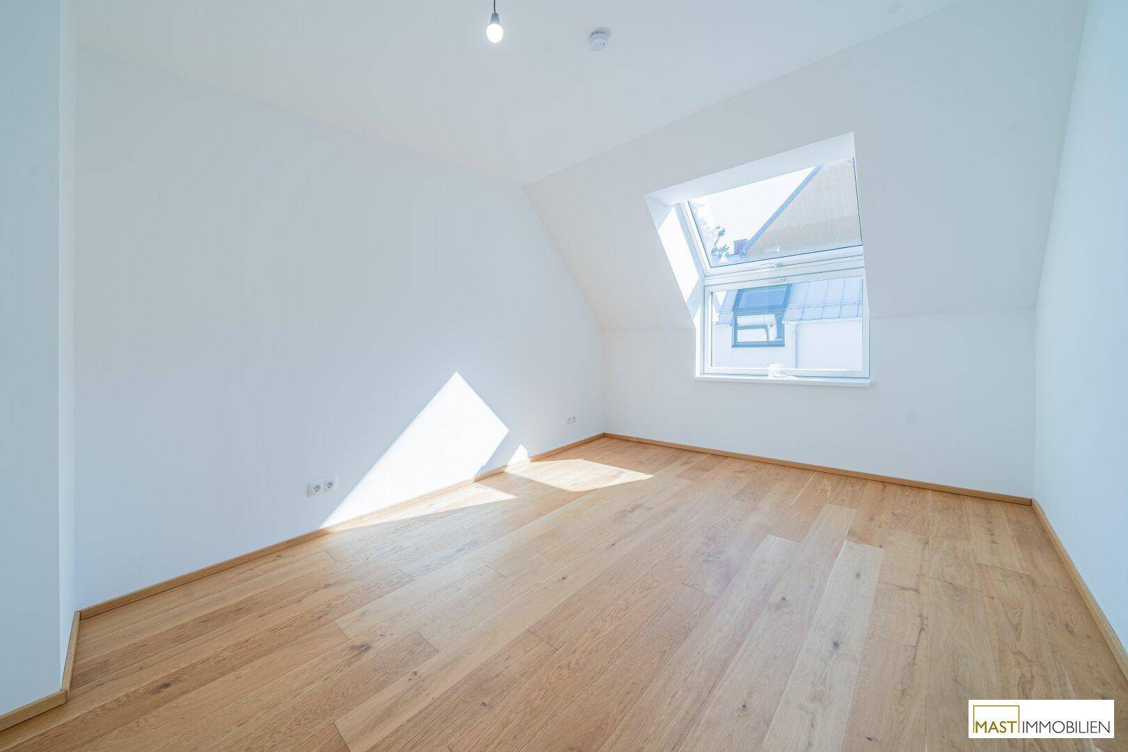 Helles Schlafzimmer im Dachgeschoss mit Holzparkettboden und großem Dachfenster.