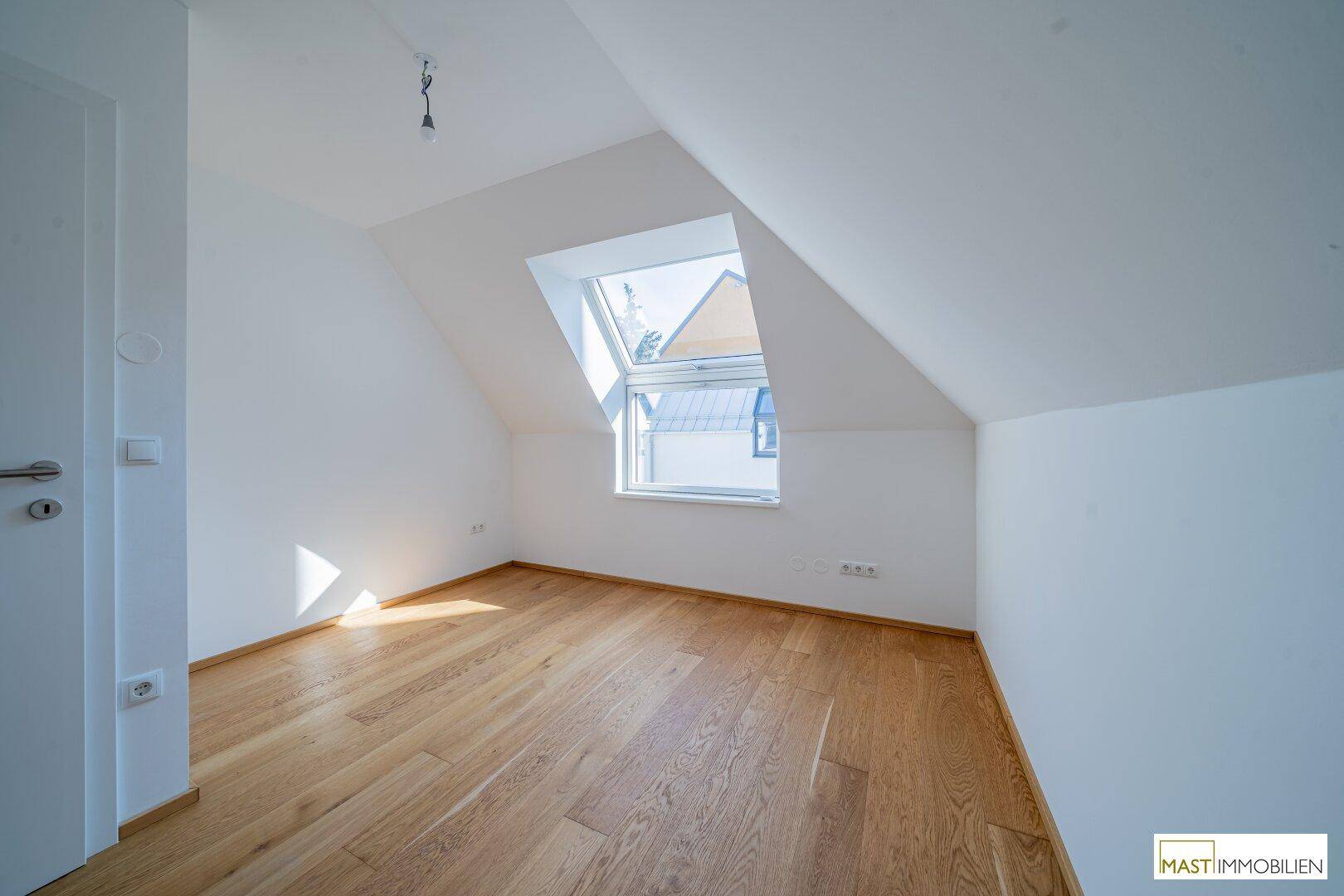 Geräumiges Schlafzimmer mit Dachschräge und viel Tageslicht durch das große Dachfenster.