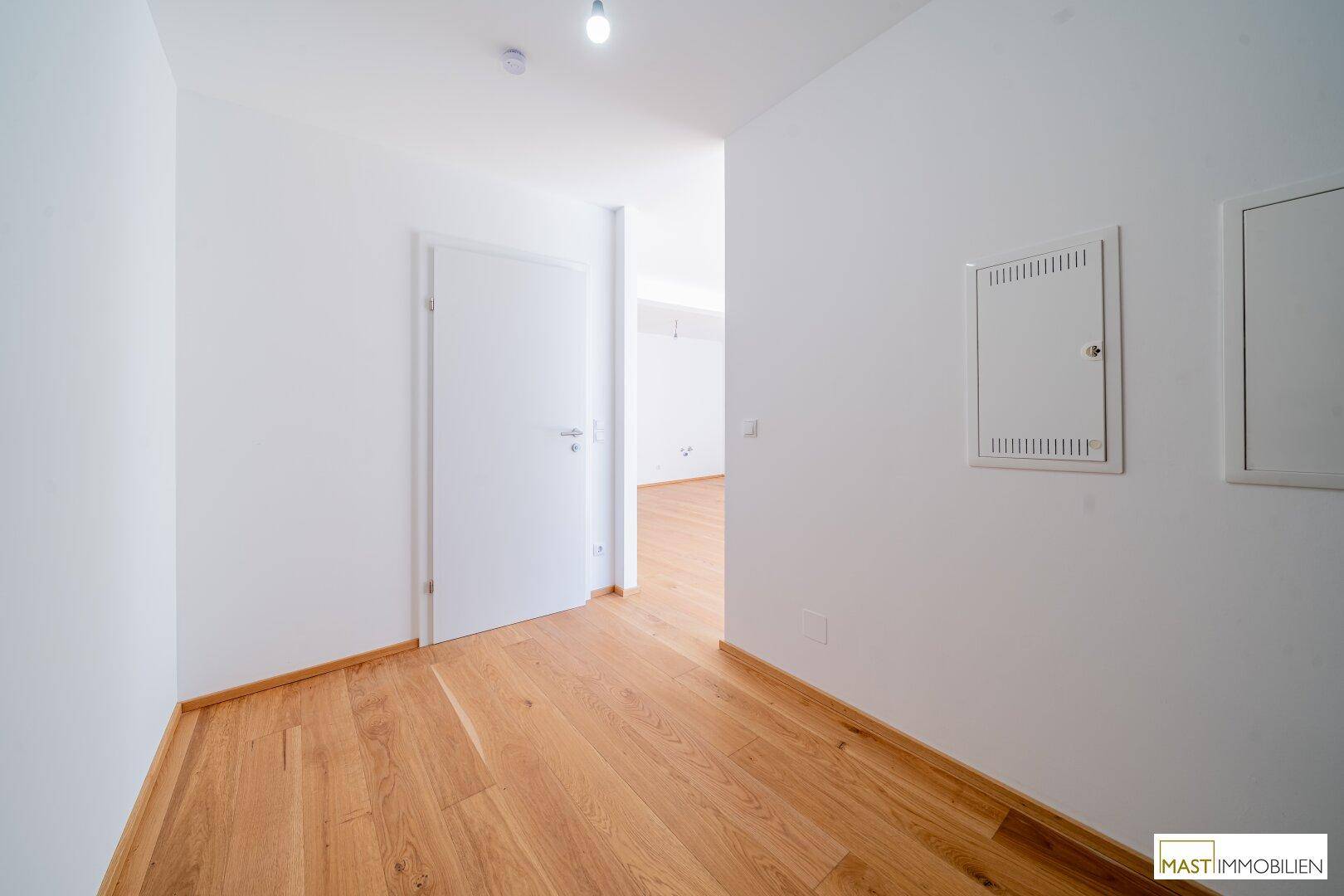 Heller Flur mit Holzparkettboden und weißen Wänden in einem modernen Neubau.
