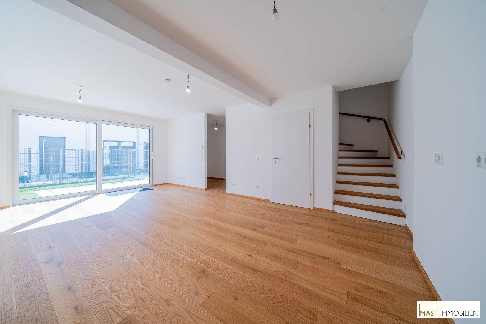 Helles Wohnzimmer mit Holzparkett und offener Treppe zum Obergeschoss.