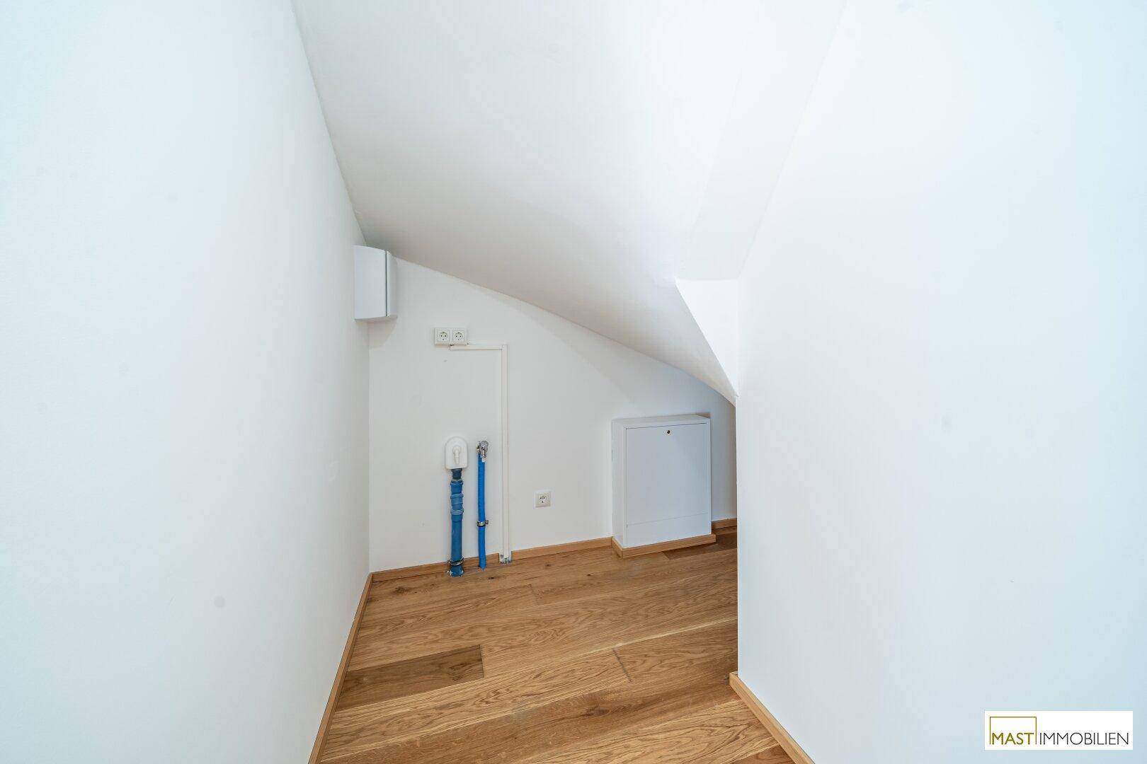 Kleiner Abstellraum mit Dachschräge, Holzparkett und Anschlüssen für Haustechnik.