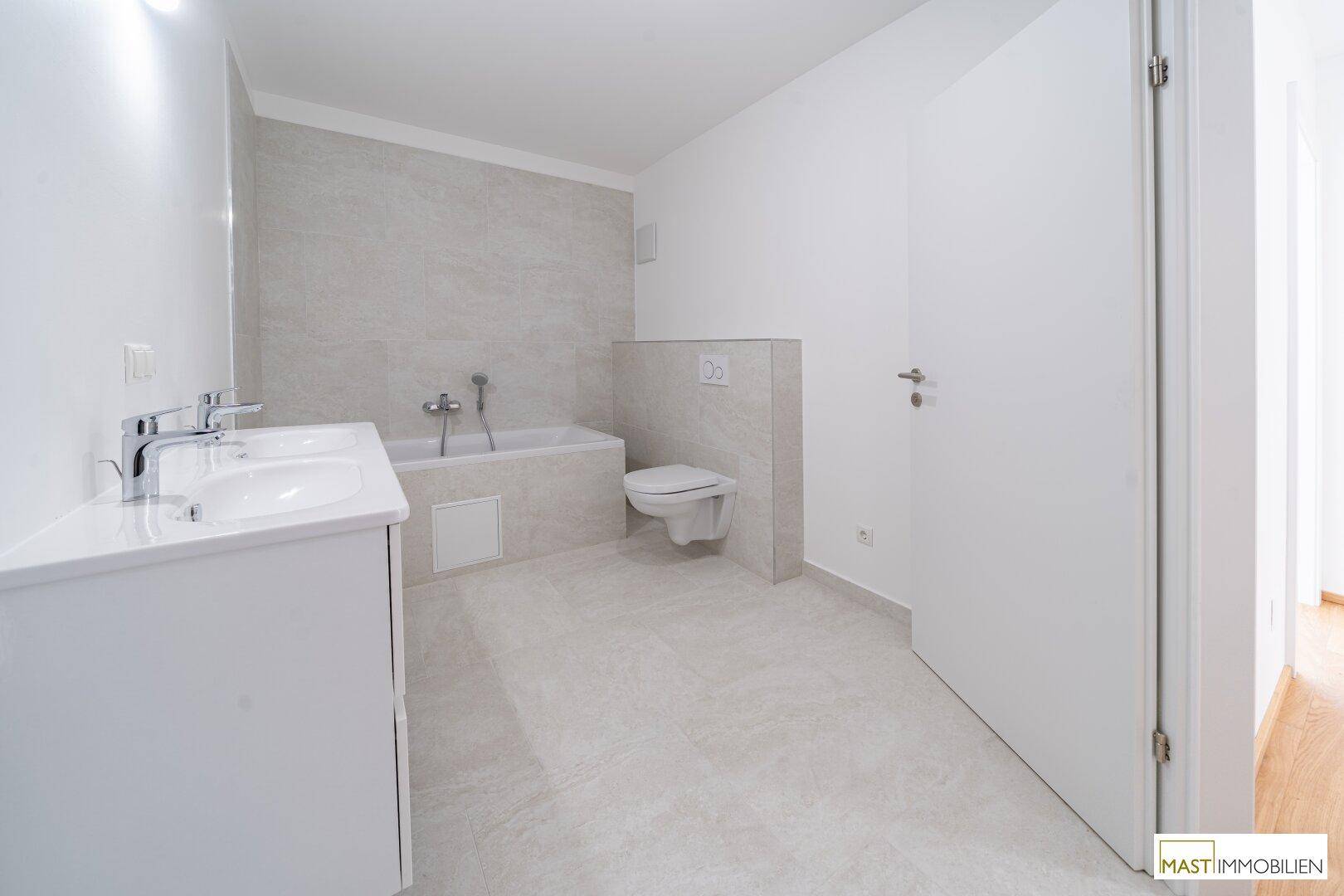 Helles Badezimmer mit Doppelwaschbecken, Badewanne und wandhängendem WC.
