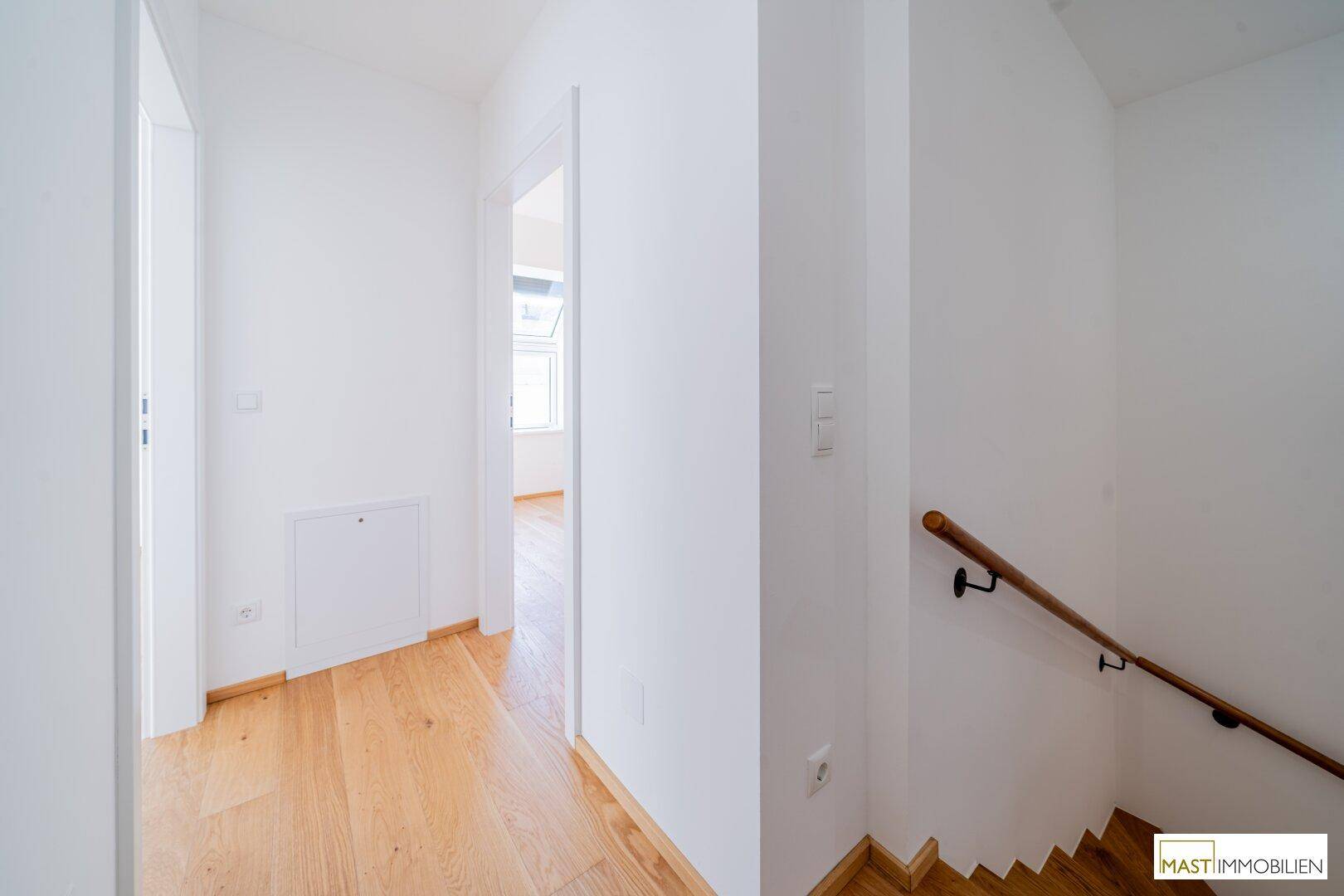 Heller Flur mit Holzparkettboden und Treppe, die in die oberen Etagen führt.