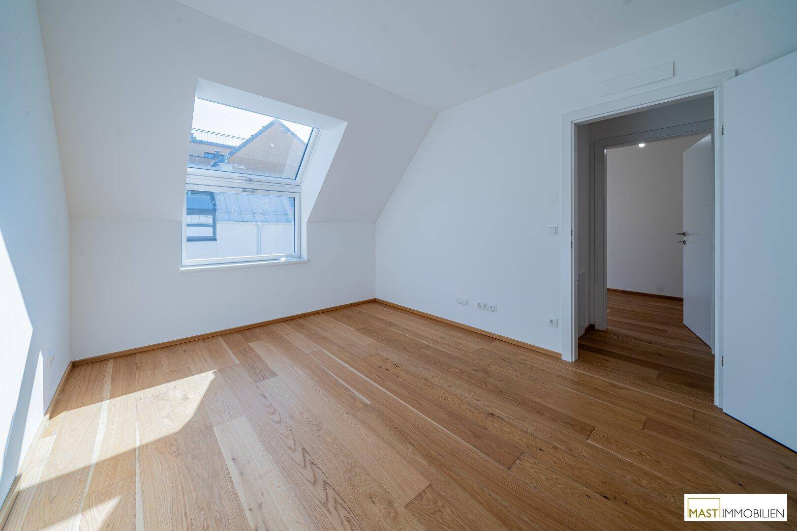 Schlafzimmer mit Dachschräge, Holzparkett und einem großen Dachfenster für viel Licht.