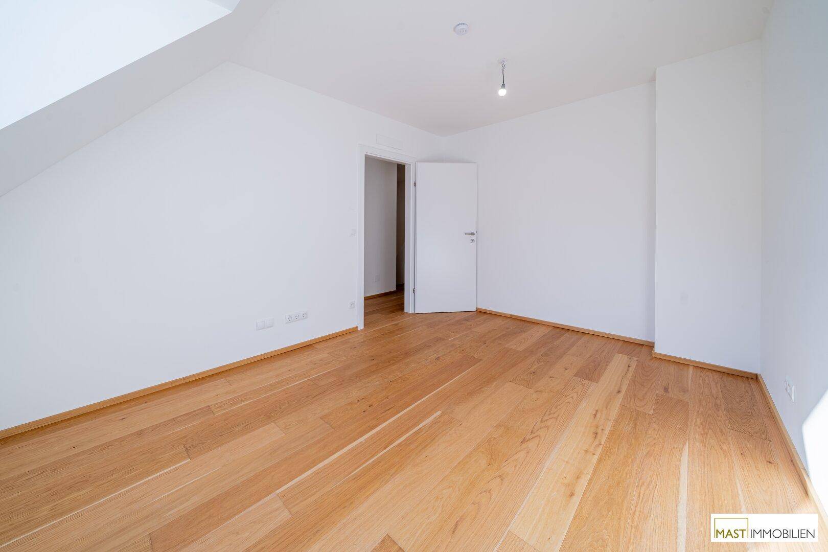 Geräumiges Schlafzimmer mit Holzparkettboden und weiß gestrichenen Wänden.