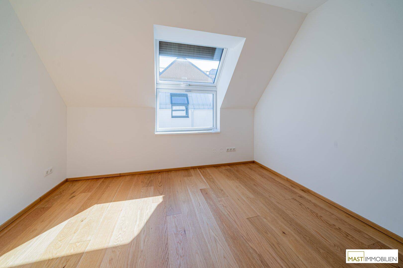 Helles Schlafzimmer mit Dachschräge und großem Dachfenster, das viel Sonnenlicht hereinlässt.