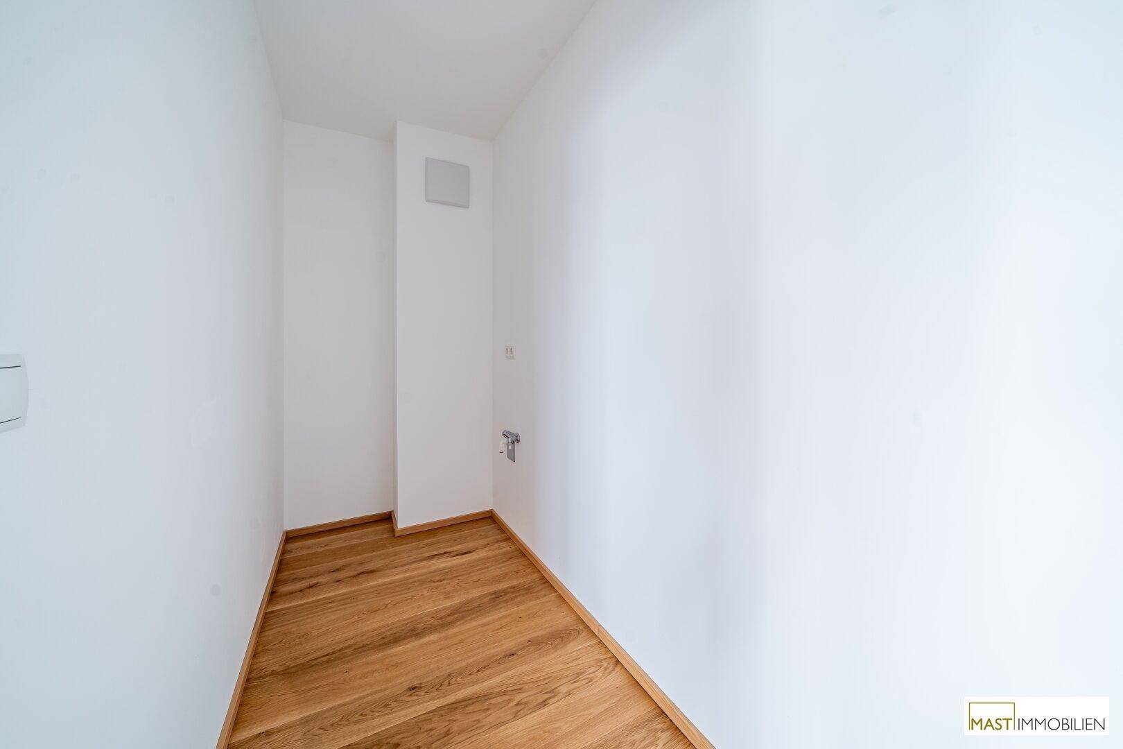 Kleiner Hauswirtschaftsraum mit Anschlüssen und Holzfußboden, ideal für Waschmaschine.