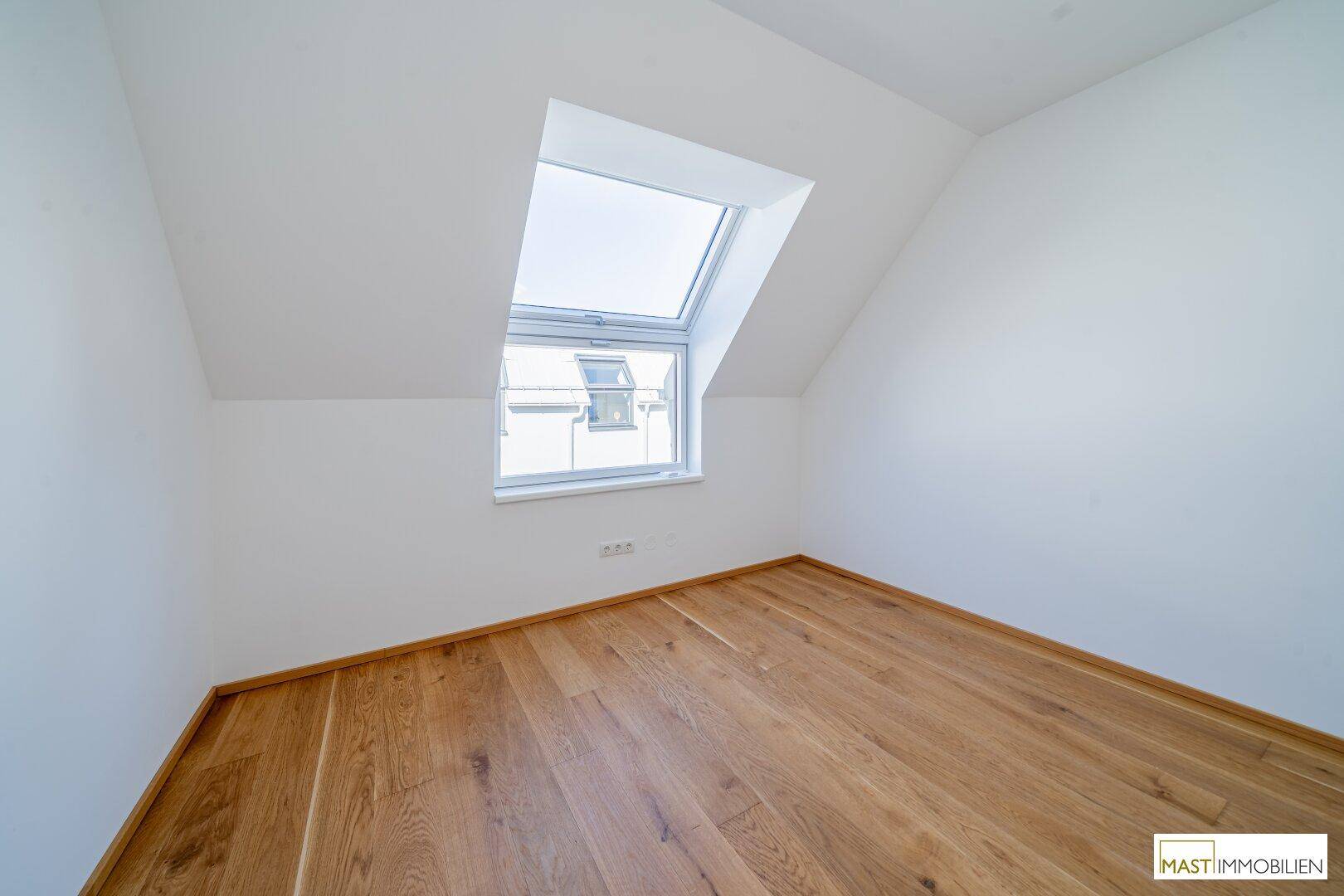 Helles Schlafzimmer im Dachgeschoss mit schräger Decke und großem Dachfenster.