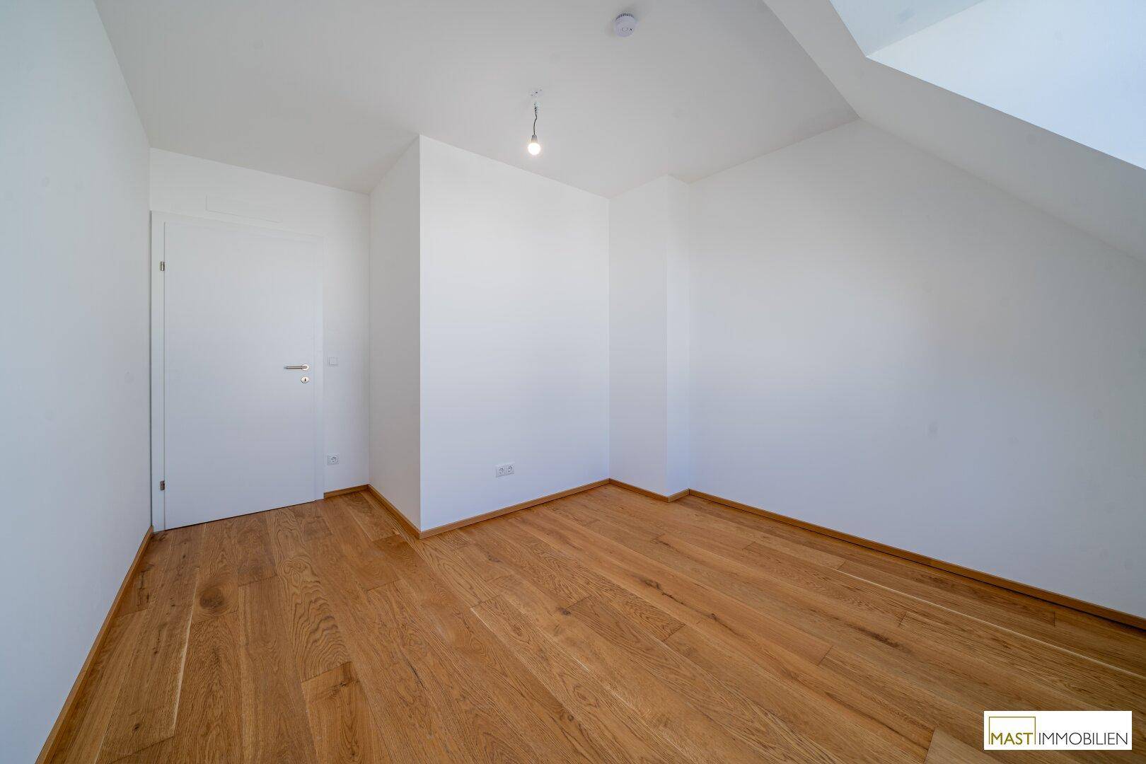 Geräumiges Schlafzimmer mit Holzfußboden und schräger Decke, bereit zur individuellen Gestaltung.