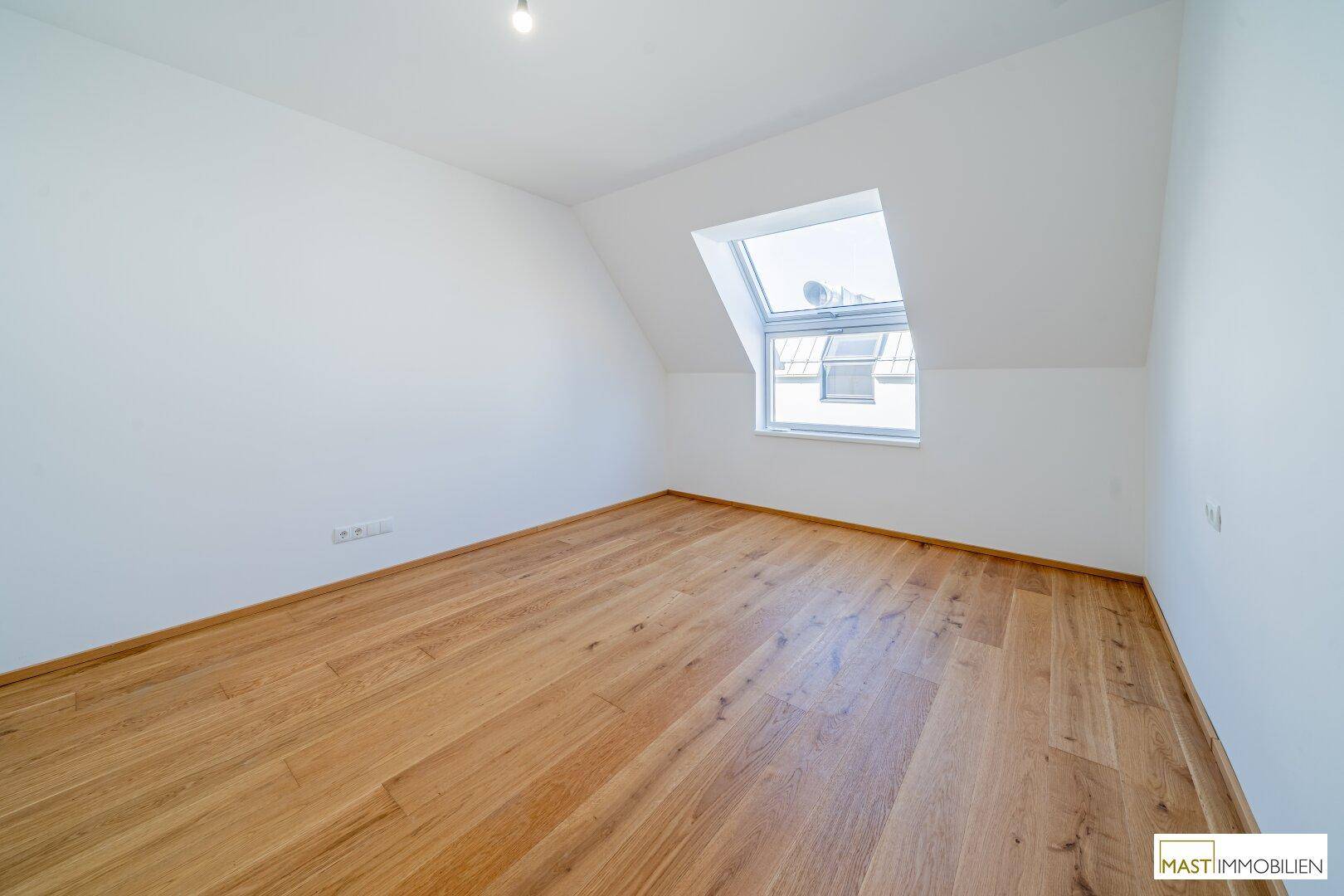 Lichtdurchflutetes Schlafzimmer im Dachgeschoss mit Holzfußboden und Dachfenster.