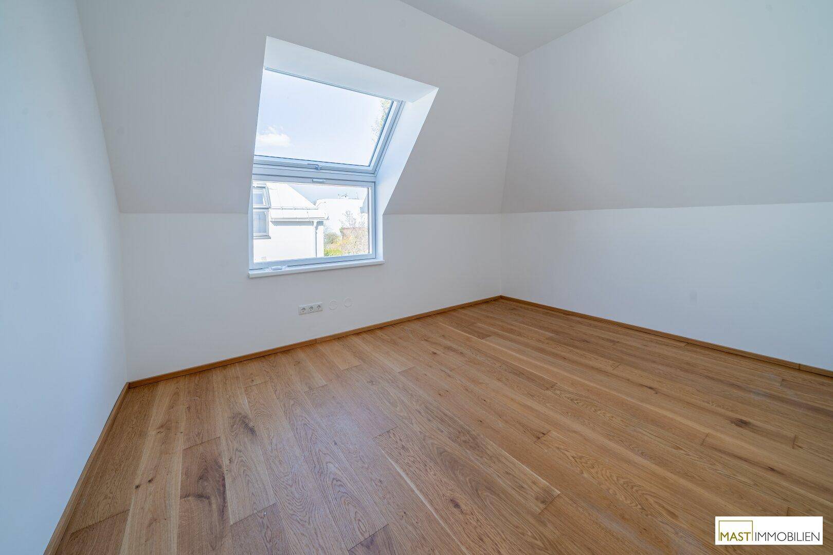 Helles Zimmer mit schräger Decke und großem Dachfenster, ideal als Kinder- oder Arbeitszimmer.