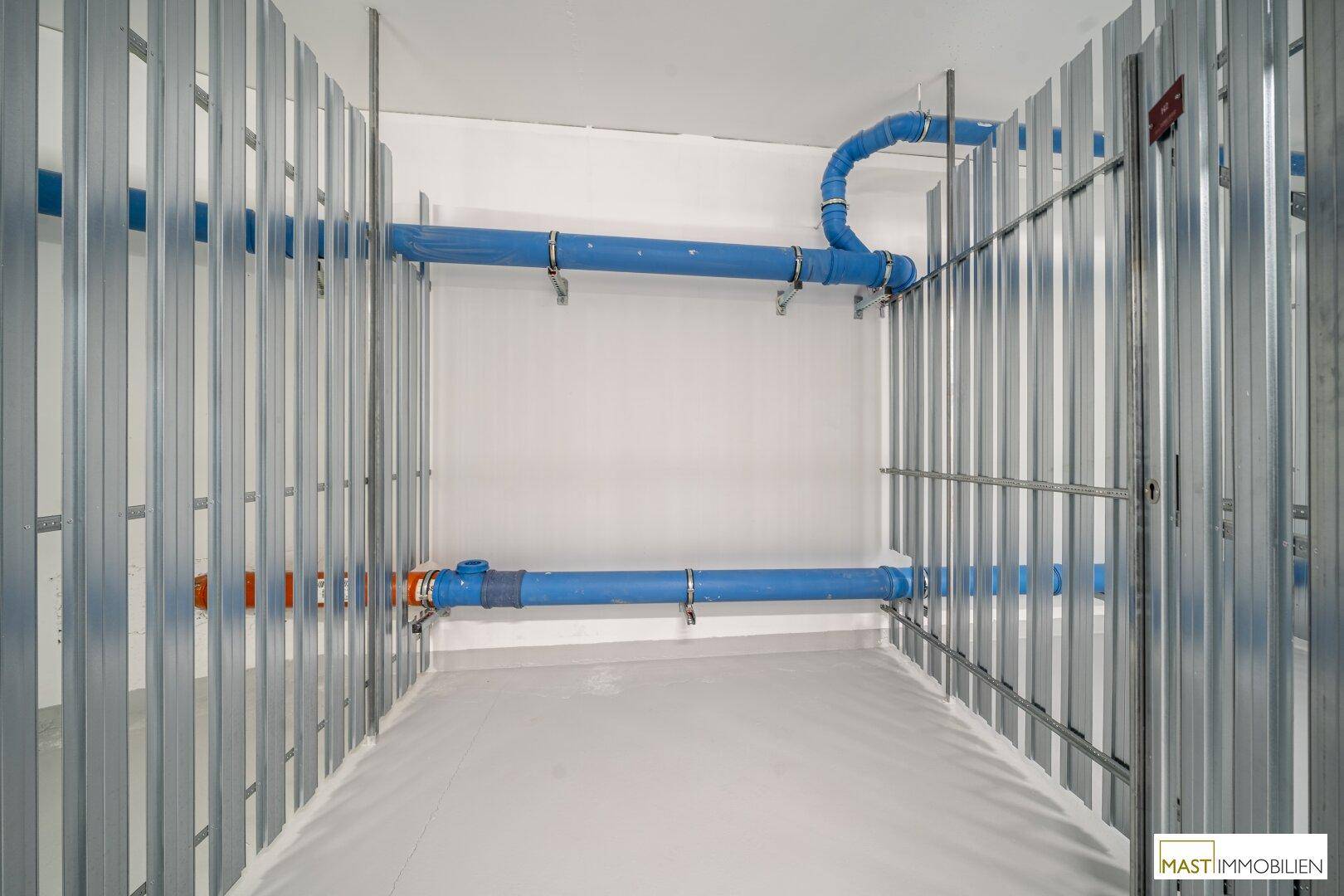 Detailansicht eines Kellerabteils mit blauen Wasserleitungen und Metallkonstruktion.