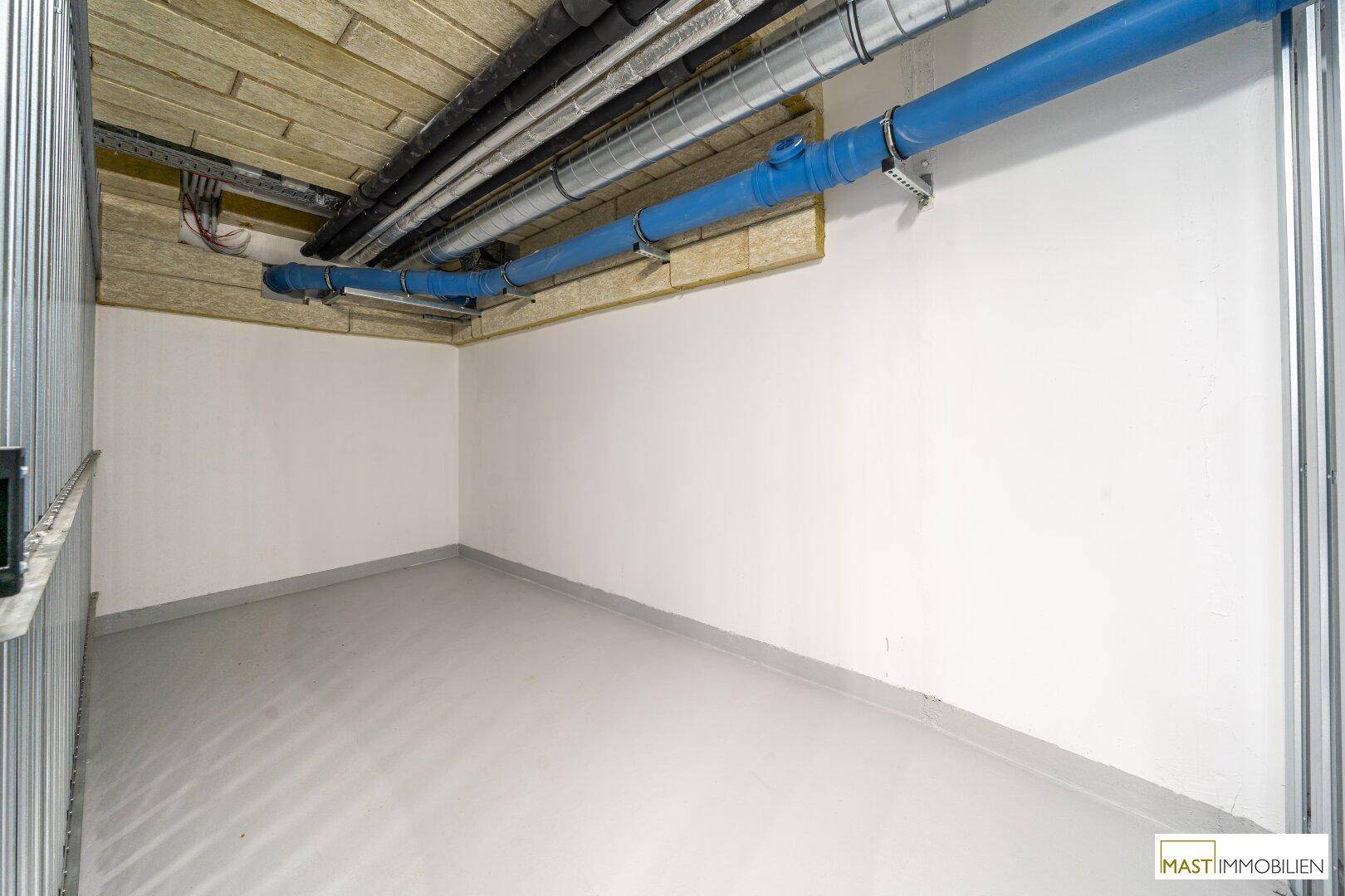 Geräumiger Kellerabteil mit Betonboden und sichtbaren Rohren an der Decke.