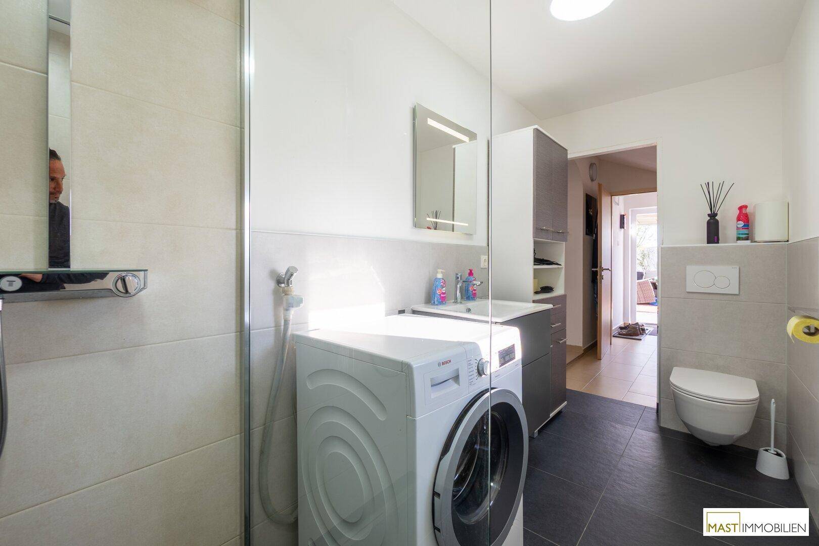Modernes Badezimmer mit Dusche, WC, Waschbecken und integrierter Waschmaschine.