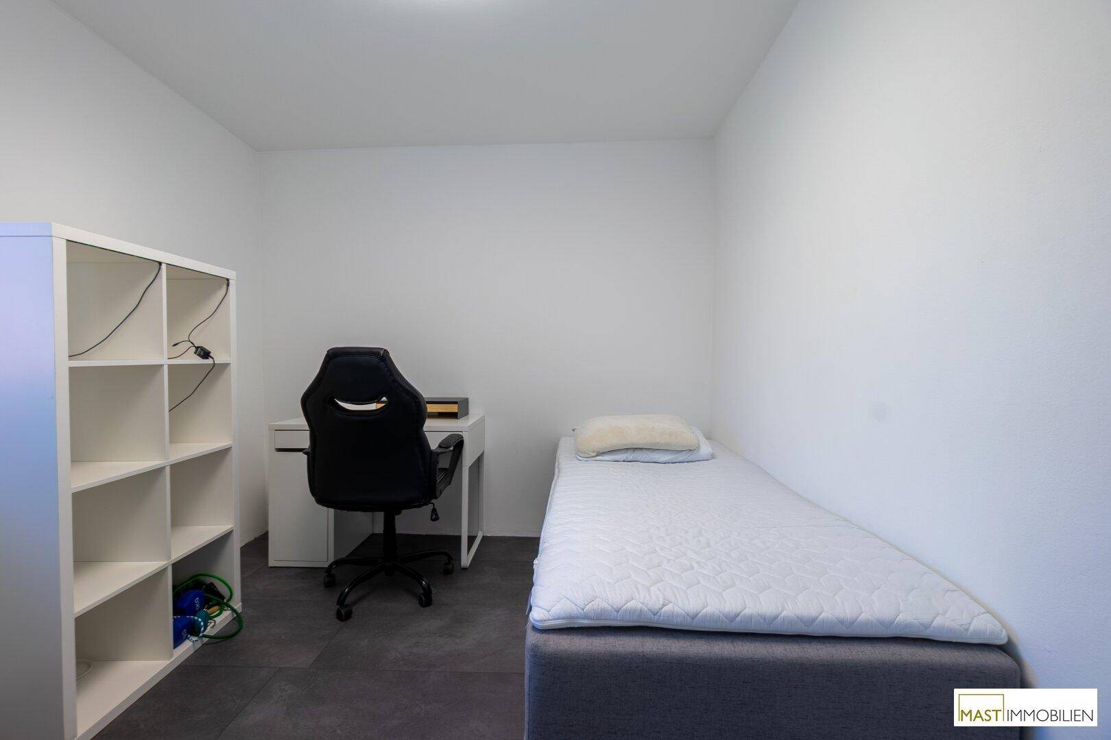 Kleines Zimmer mit Einzelbett, Schreibtisch und Regal, ideal als Gäste- oder Kinderzimmer.