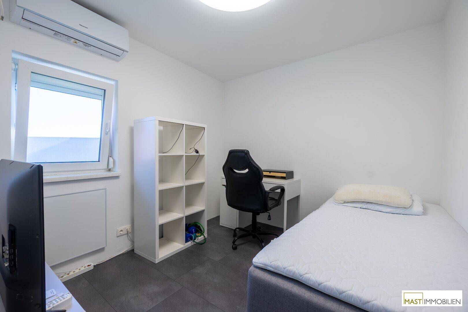 Helles Zimmer mit Fenster, Einzelbett, Schreibtisch und Klimaanlage.