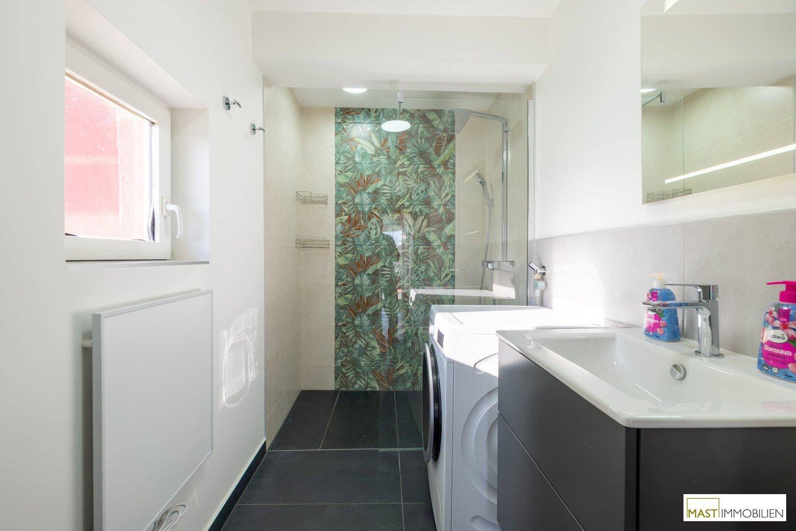Badezimmer mit Fenster, Dusche mit dekorativen Fliesen und Waschbecken.