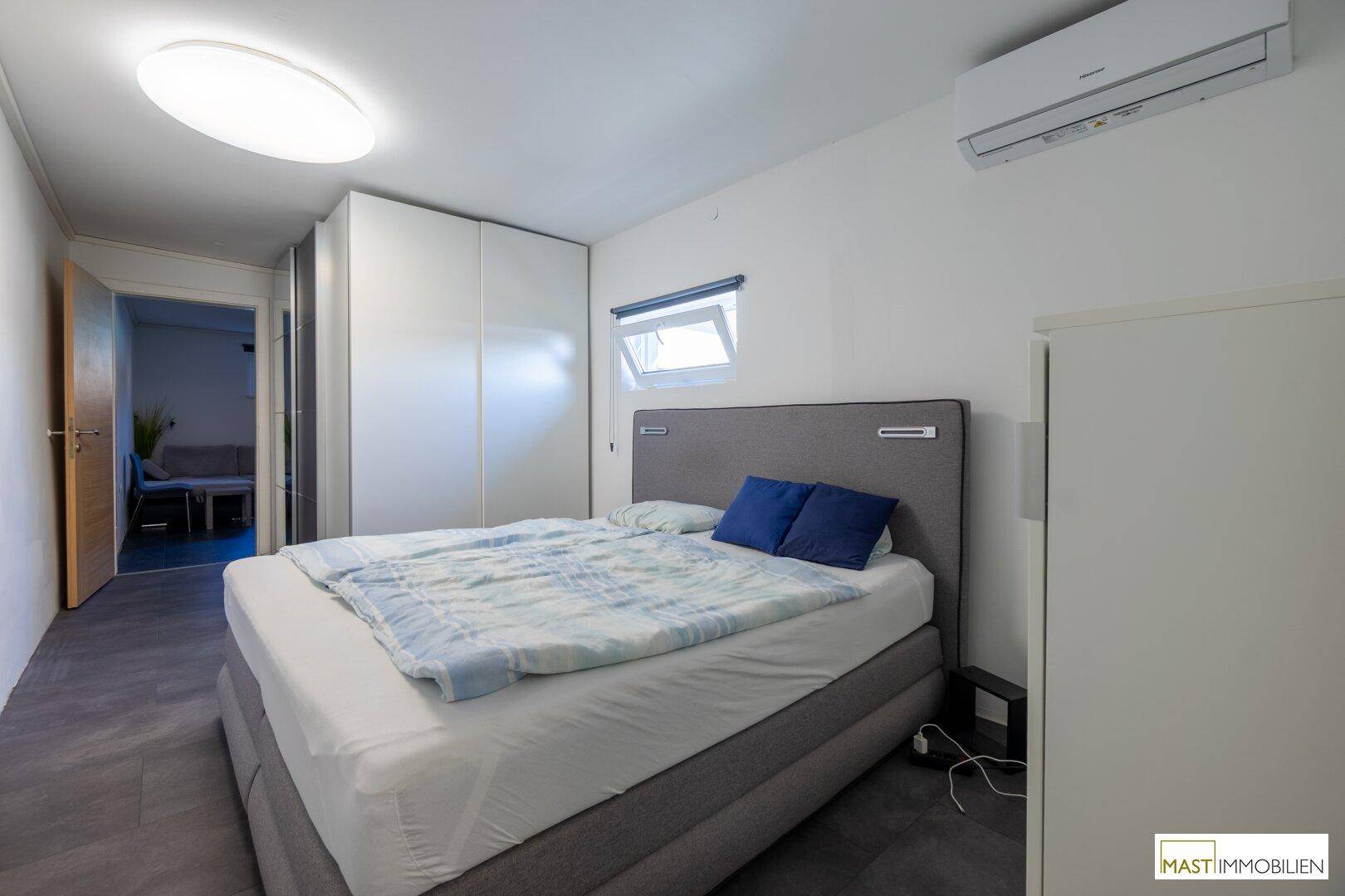 Schlafzimmer mit Doppelbett, Kleiderschrank, Klimaanlage und dunklem Fliesenboden.