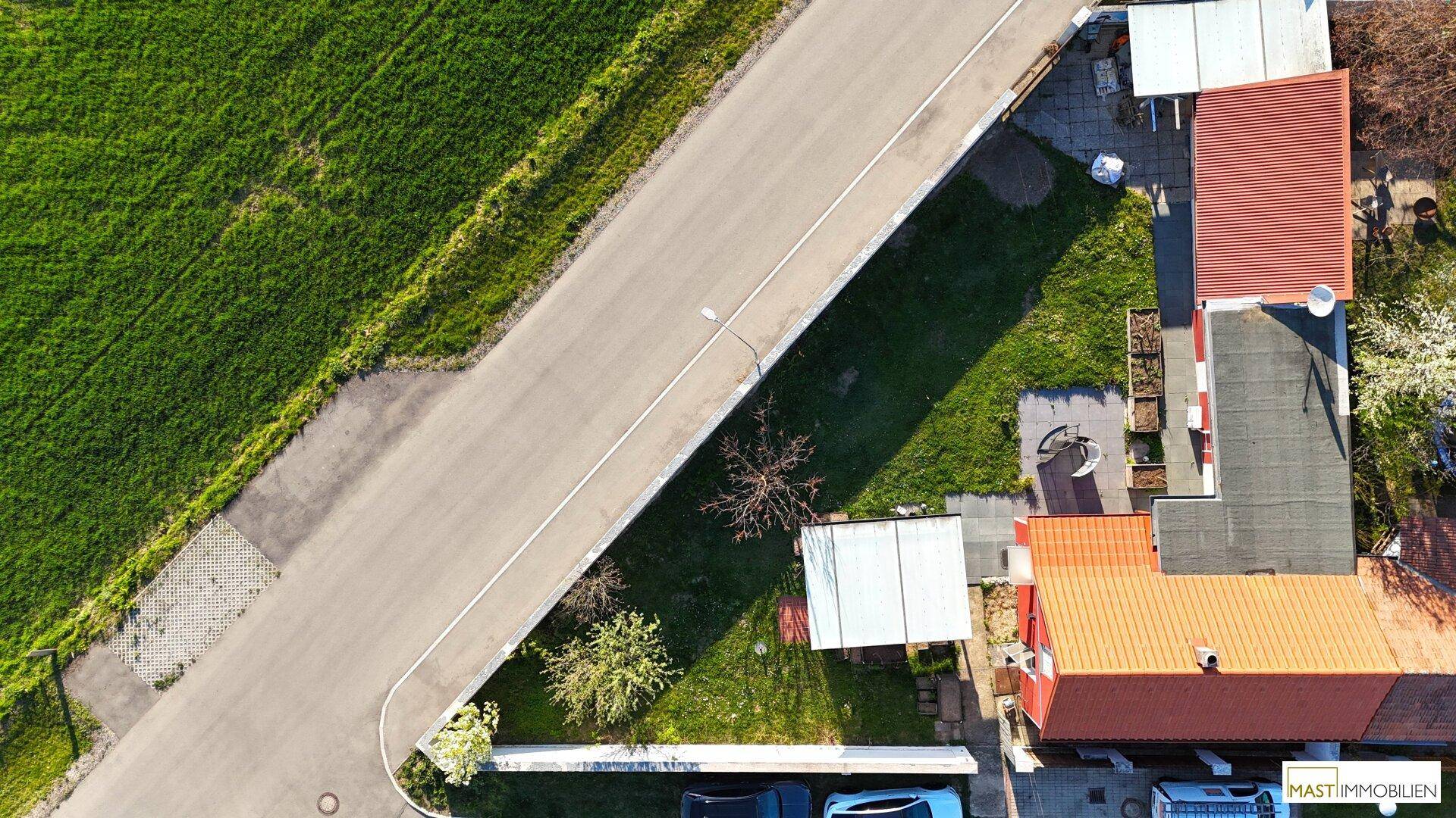 Vogelperspektive des Grundstücks mit Hausdach, Gartenbereich und angrenzender Straße.