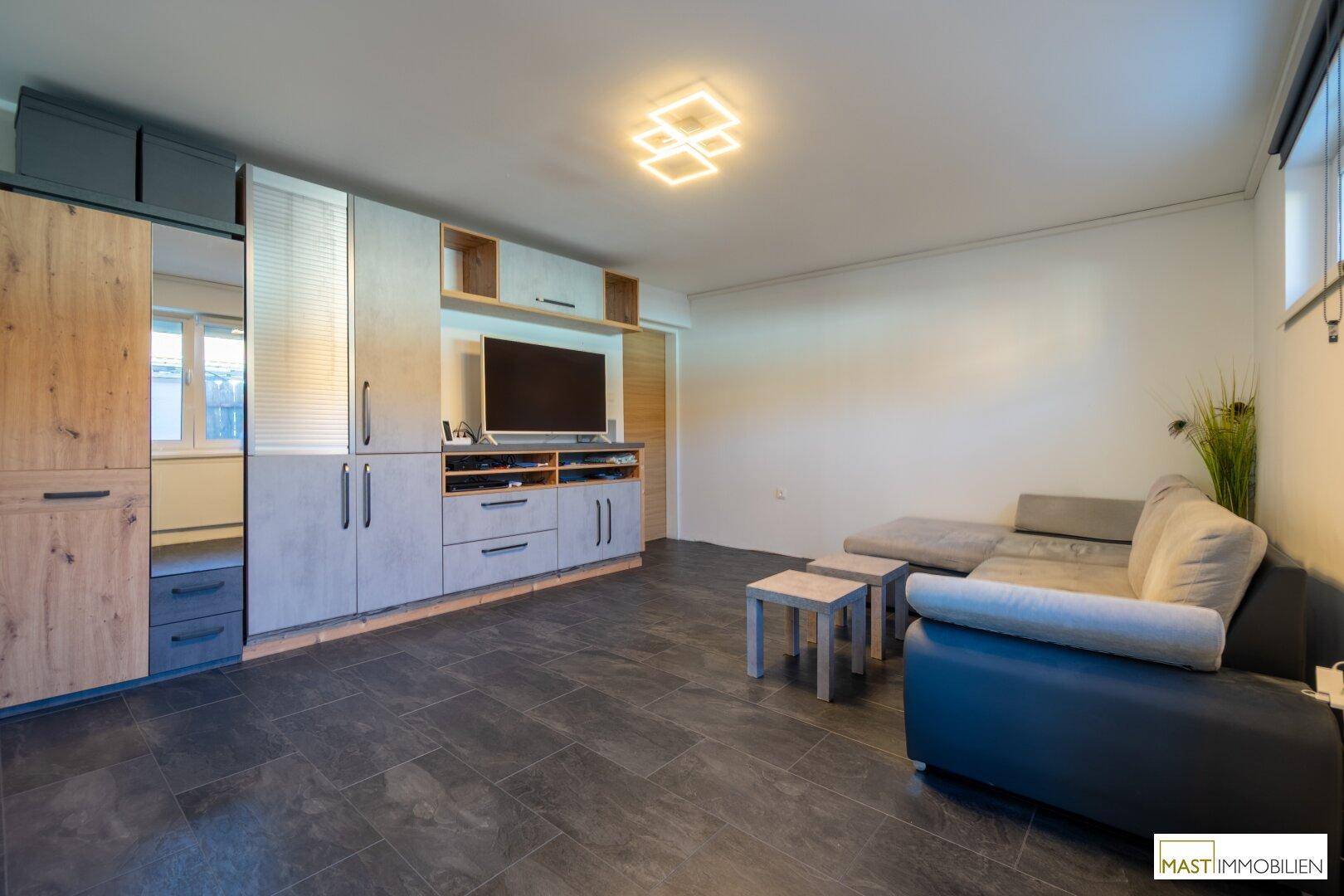 Geräumiges Wohnzimmer mit moderner Einrichtung, dunklem Fliesenboden und viel Stauraum.