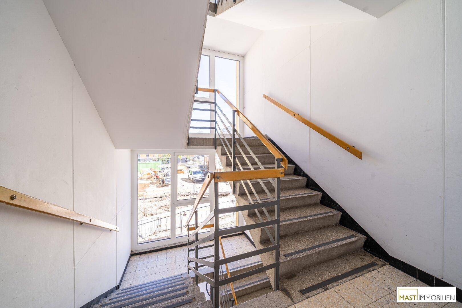 Treppenhaus mit mehreren Etagen und Fenstern, die Tageslicht hereinlassen.