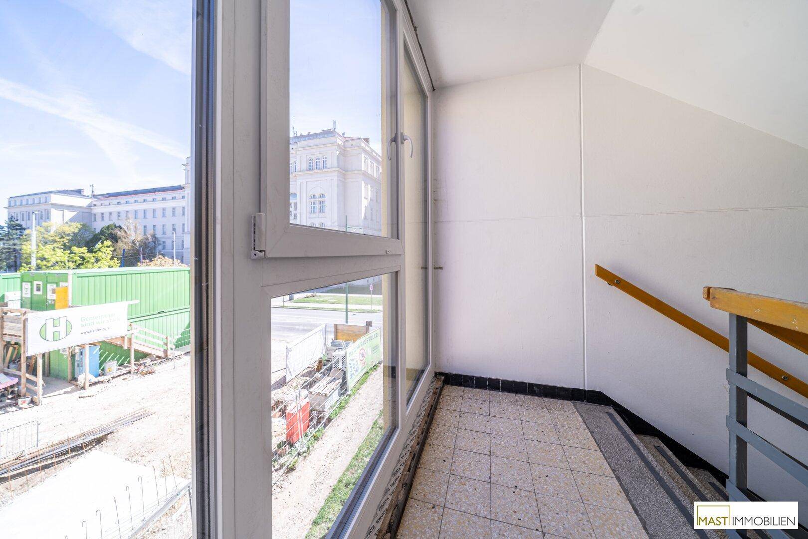 Treppenabsatz mit großem Fenster und Blick auf eine Baustelle im Außenbereich.