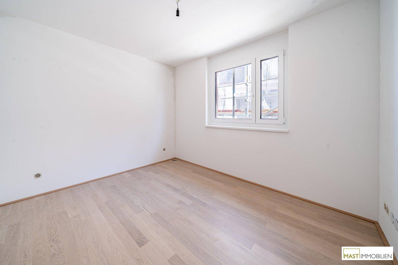 Geräumiges Schlafzimmer mit hellem Parkettboden und einem Fenster, das für gute Belichtung sorgt.