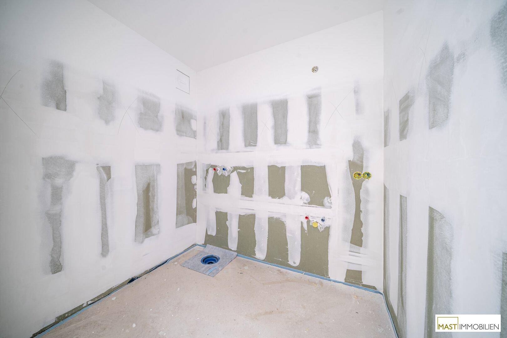 Badezimmer im Rohbau mit vorbereiteten Installationen für Dusche oder Badewanne.