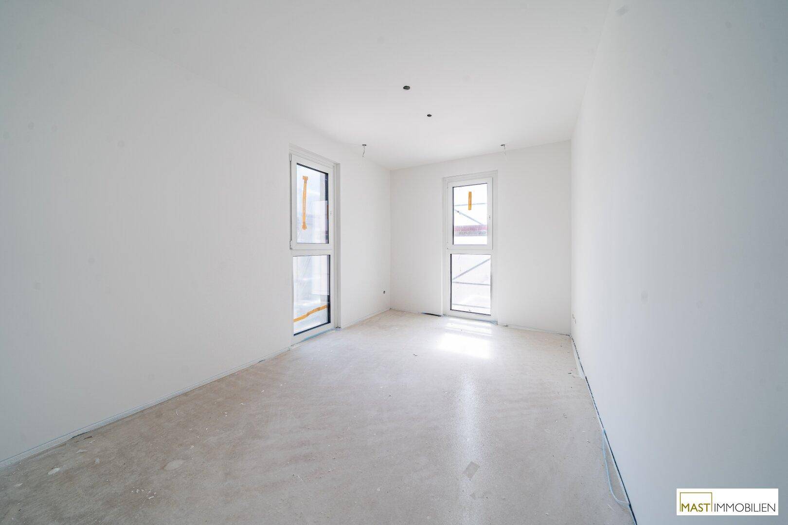 Unfertiges Zimmer mit viel Tageslicht durch zwei Fenster, bereit für den Innenausbau.