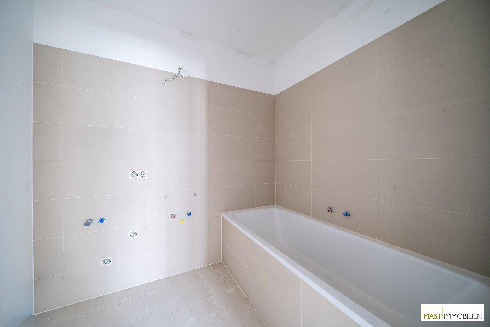 Modernes Badezimmer im Bau mit Badewanne und hellen Fliesen, noch ohne Armaturen.