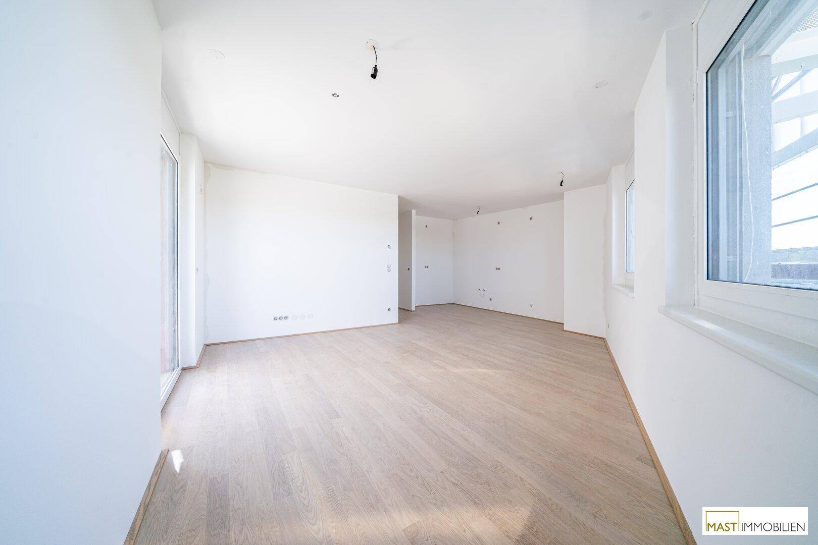 Heller, leerer Raum mit Parkettboden und großen Fenstern, ideal für ein Wohnzimmer.