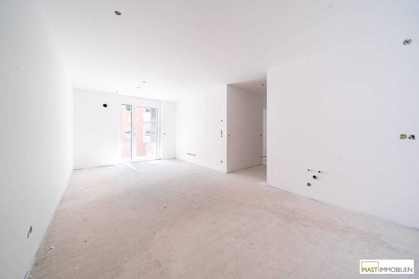 Heller, unmöblierter Raum im Rohbau mit großen Fenstern und Betonboden, bereit für den Ausbau.
