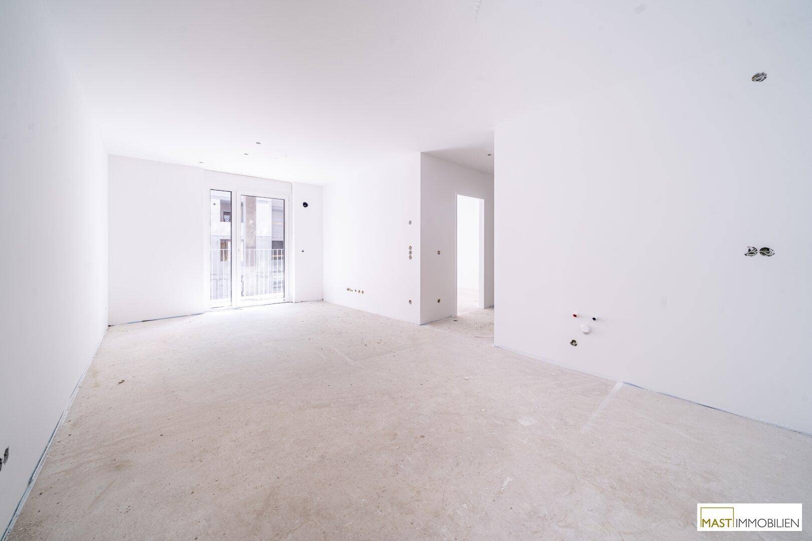 Heller, unmöblierter Raum mit weißen Wänden, Betonboden und Zugang zu einem Balkon oder einer Terrasse.