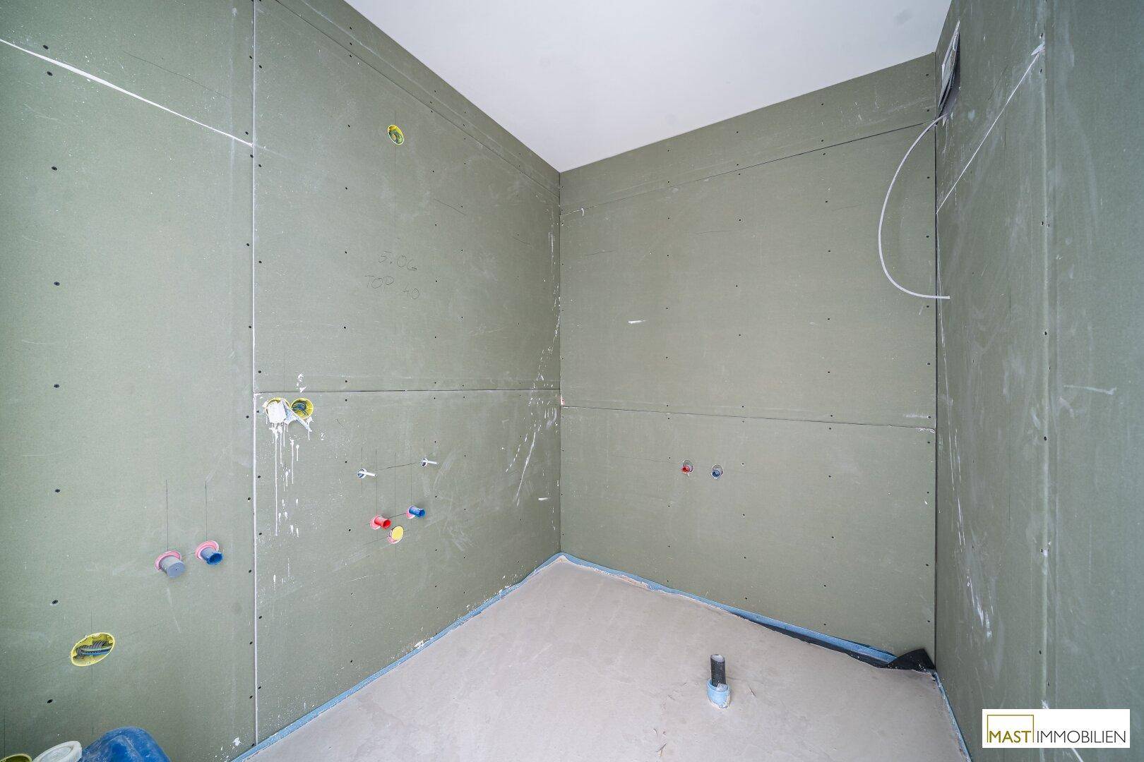 Badezimmer im Rohbau mit vorbereiteten Anschlüssen für Sanitärinstallationen und Wänden.