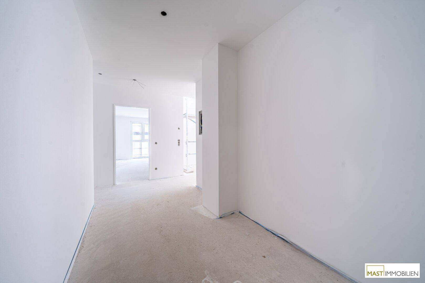 Unfertiger Flur in einem Neubau mit weißen Wänden und Rohbetonboden, bereit für den Ausbau.