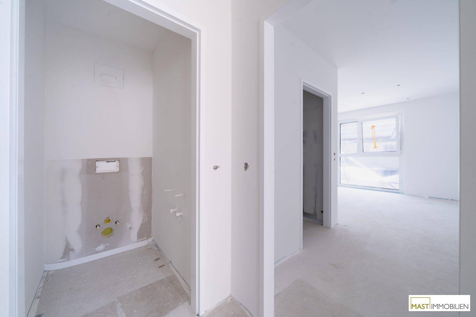 Heller Flur in einem Neubau mit vorbereiteten Anschlüssen für ein WC oder einen Abstellraum.