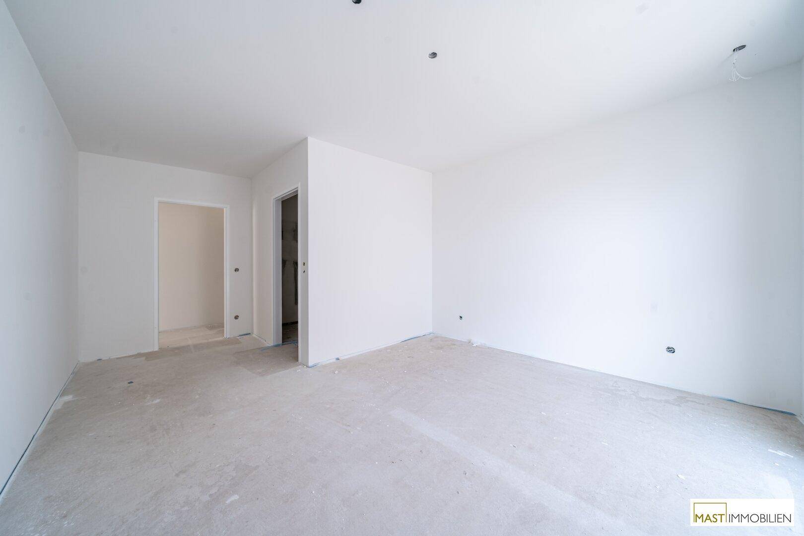 Heller, unfertiger Raum in einem Neubau mit weißen Wänden und Rohbetonboden.