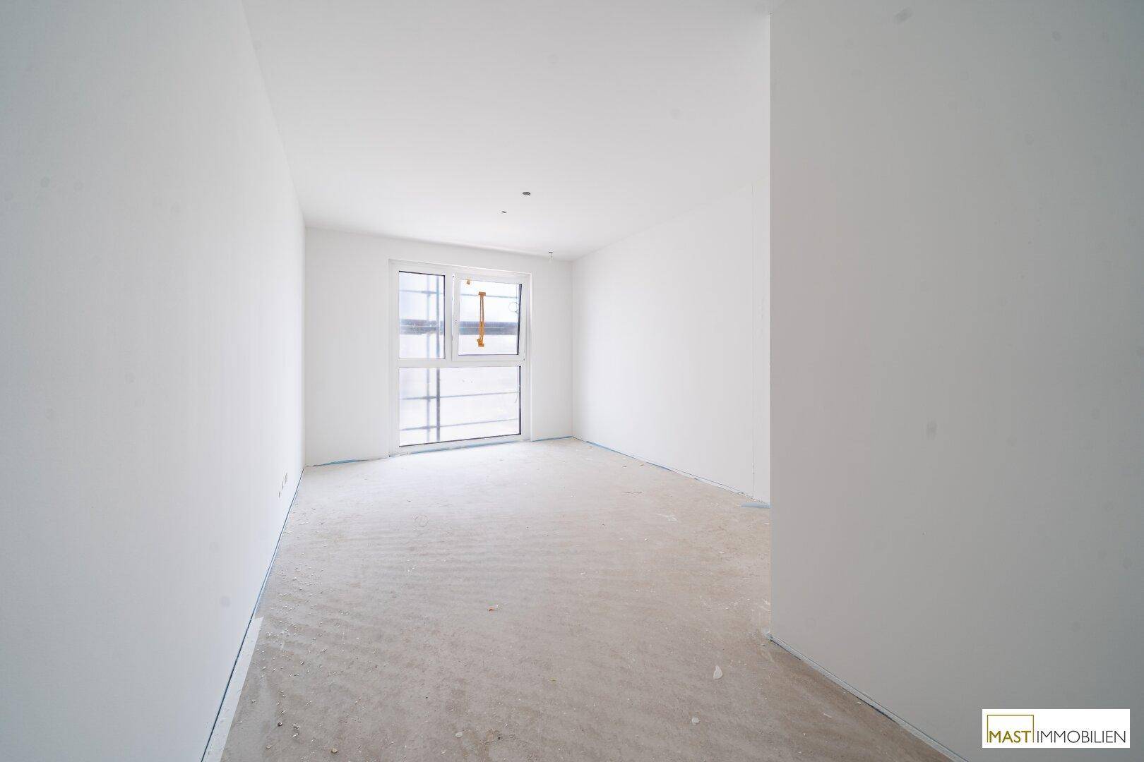 Helles, unfertiges Schlafzimmer in einem Neubau mit Fenster und Rohbetonboden.