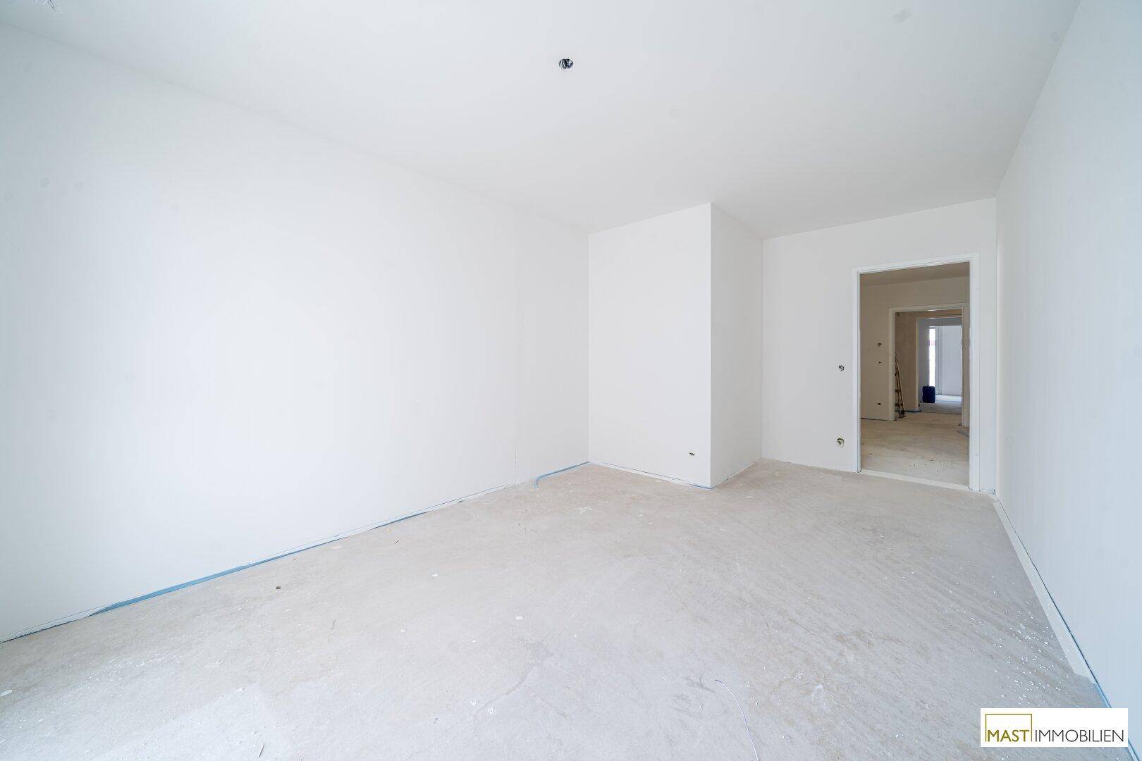 Unfertiger Raum in einem Neubau mit weißen Wänden und Rohbetonboden, bereit für den Ausbau.