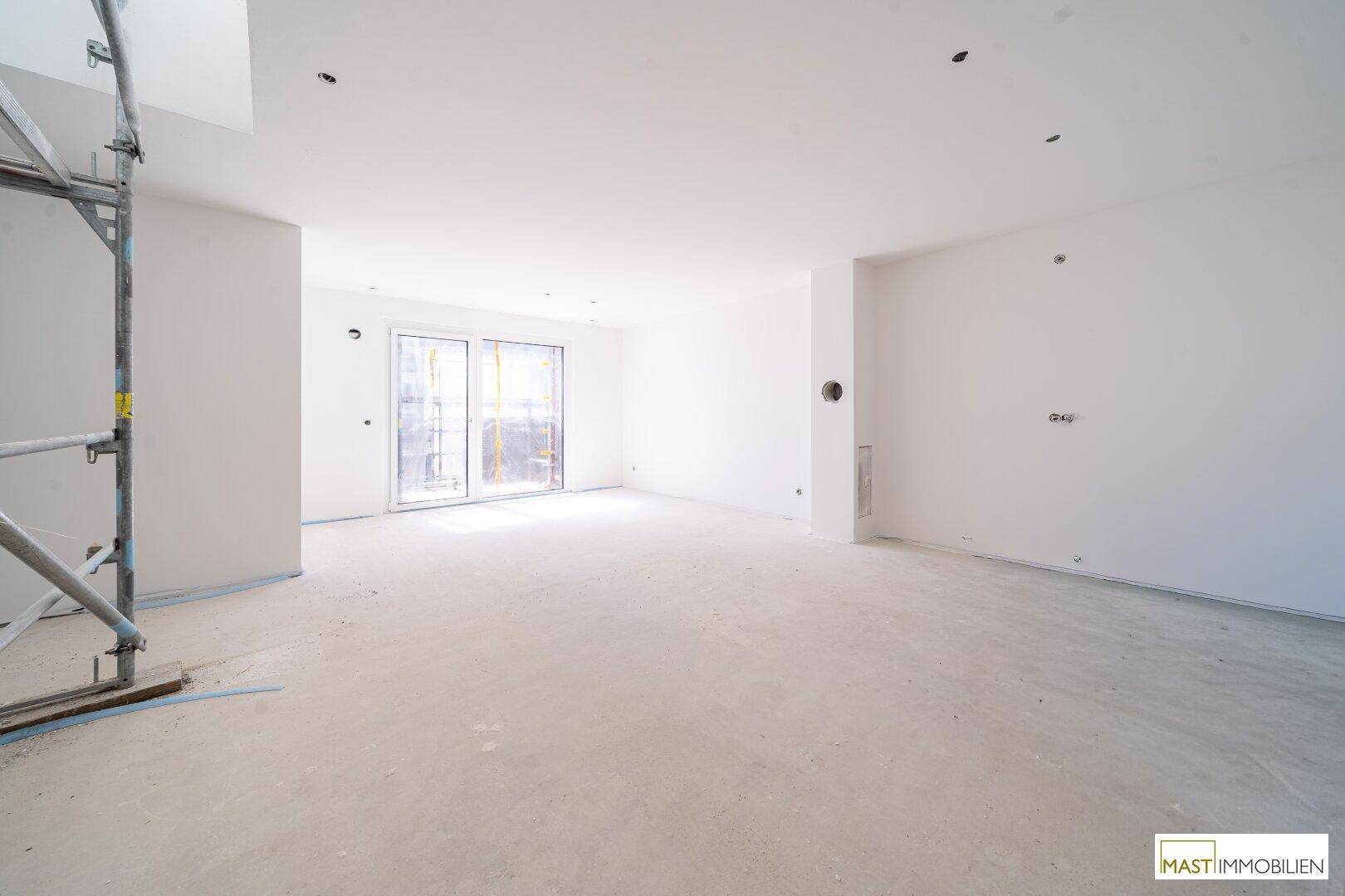 Geräumiger, unfertiger Wohnbereich in einem Neubau mit großen Fenstern und viel Tageslicht.