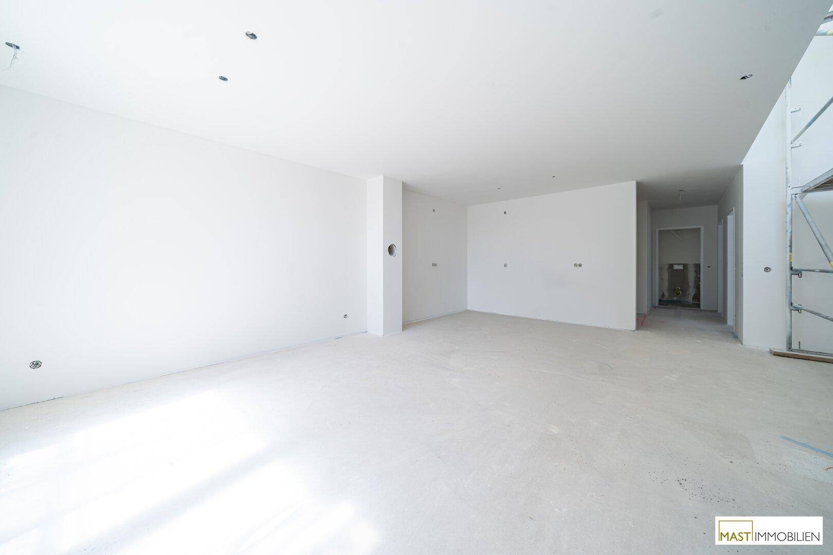 Heller, unfertiger Wohnbereich in einem Neubau mit weißen Wänden und Rohbetonboden.